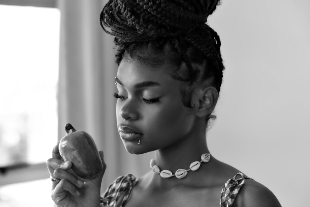 Black and white portrait of a woman holding a cashew fruit indoors.